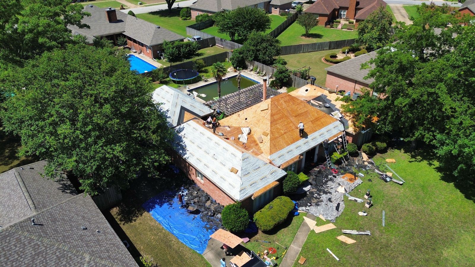 Precision Roofing Alabama crew at work on an Alabama roof with decking exposed for inspection and the landscaping protected by tarps