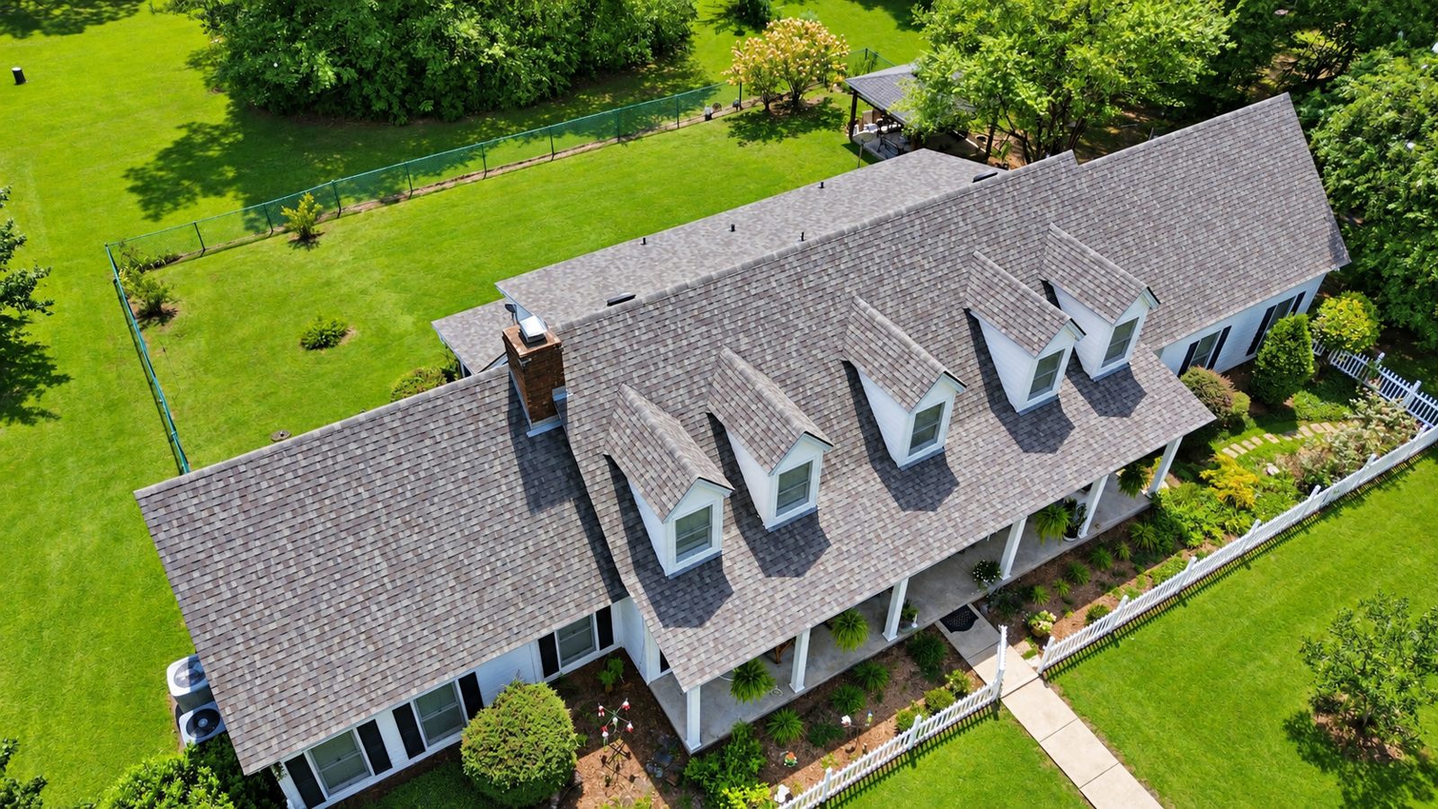 Aerial view of a completed CertainTeed Weathered Wood shingle roof replacement in Pike Road, Alabama on a white home with five dormers and a full-length front porch